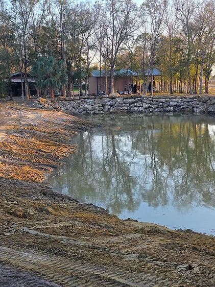 Cleared waterfront lot with rock-lined bank and mature trees, ready for development
