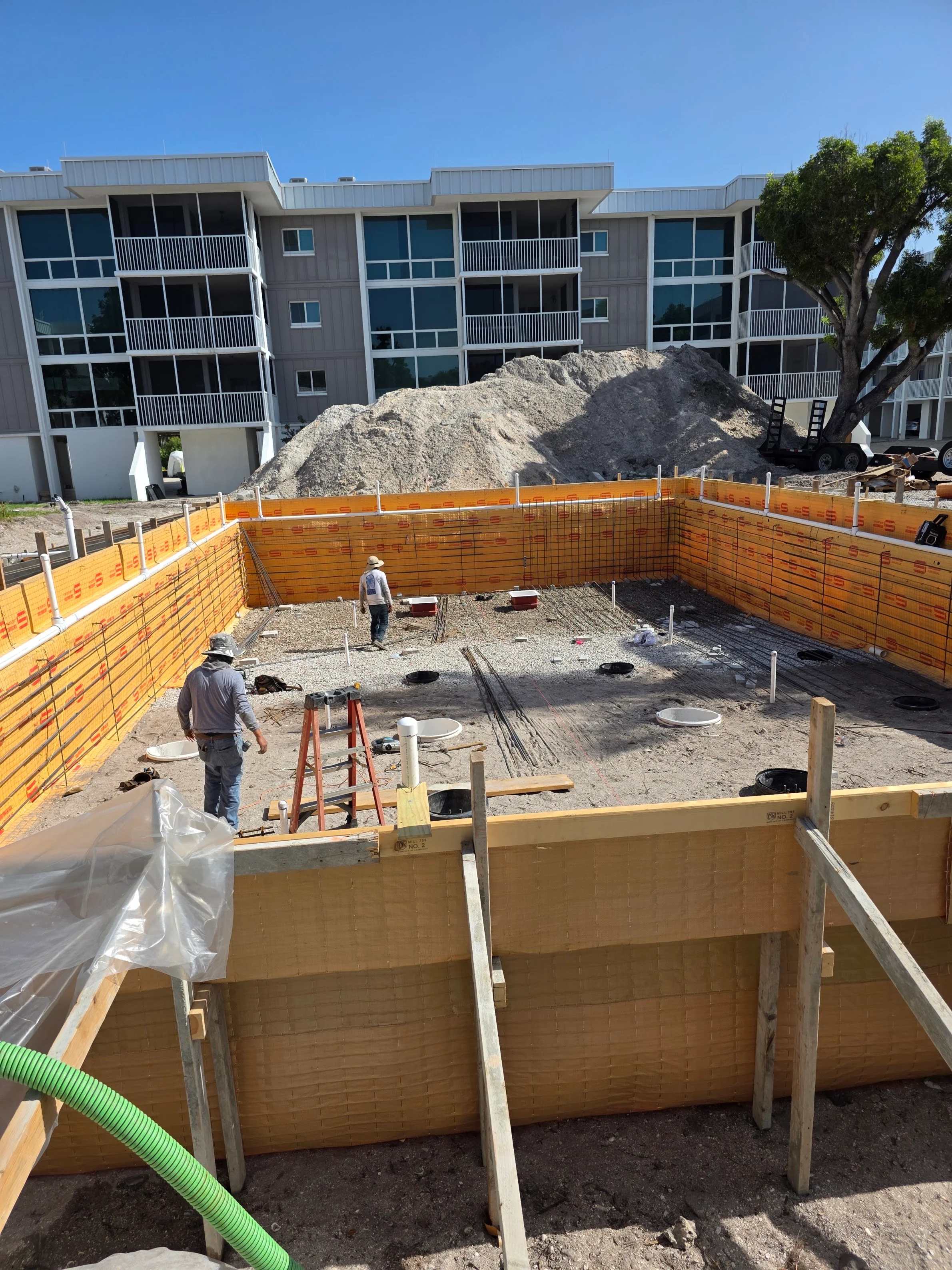 In-ground pool excavation with wooden formwork, gravel base, and utility lines at residential construction site