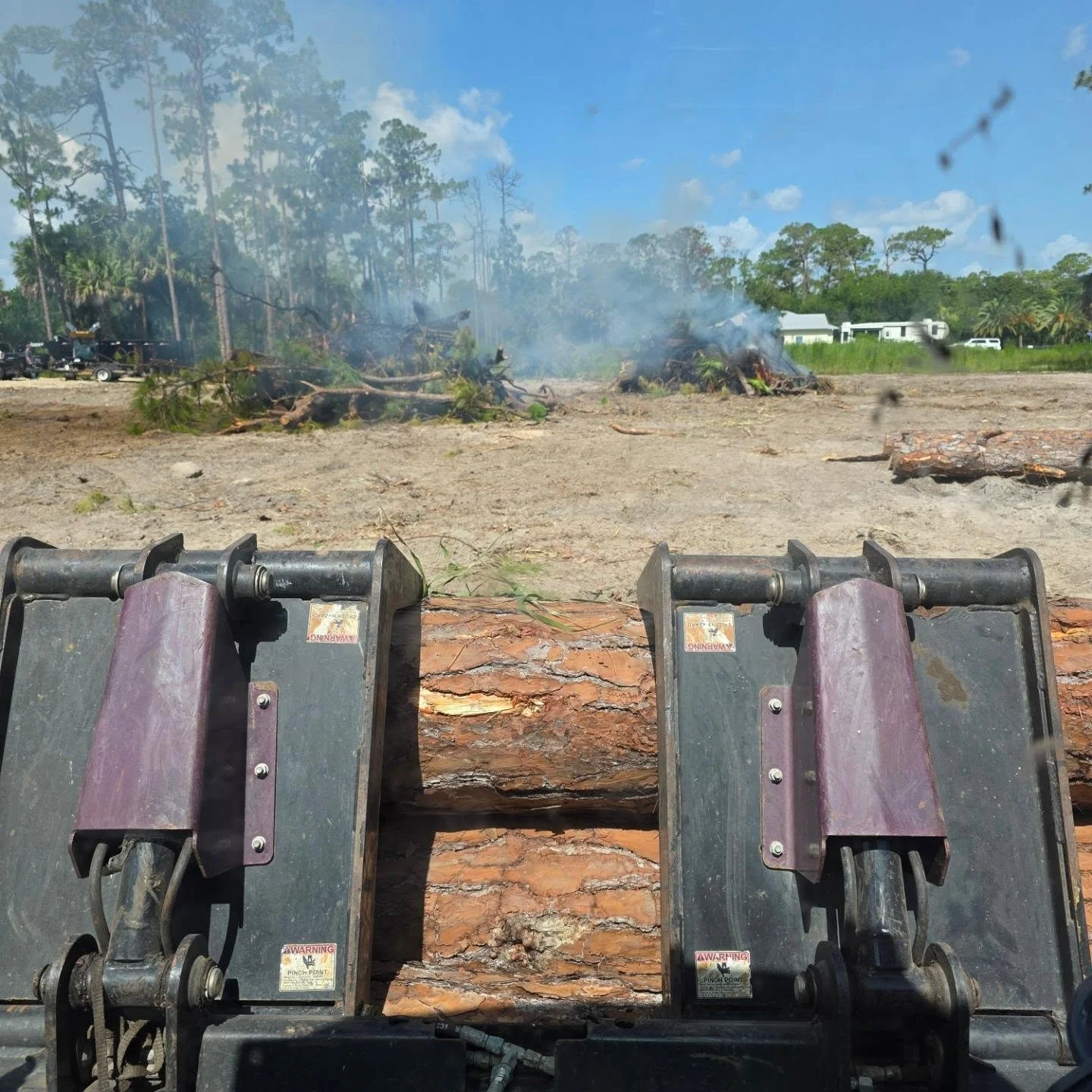 Industrial wood chippers processing logs with burning debris pile and cleared land in background