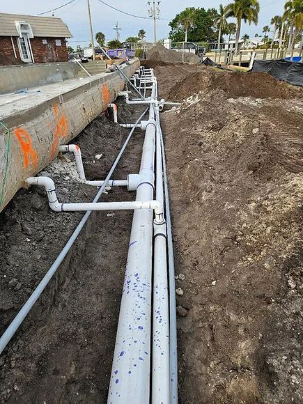 White PVC utility pipes installed in excavated trench with dirt embankment