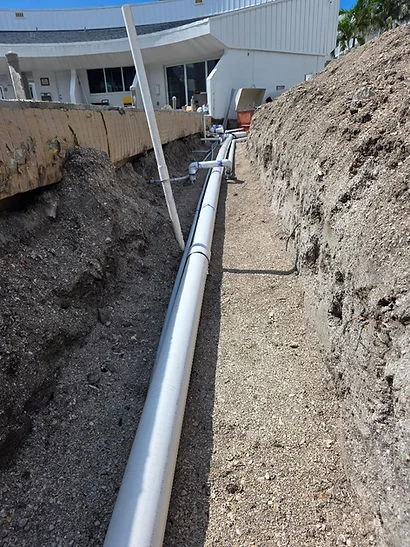 PVC drainage pipe in excavated trench with compacted soil and building foundation visible