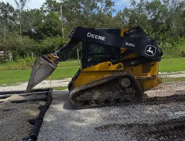 Skid steer loader spreading gravel on driveway with bucket attachment