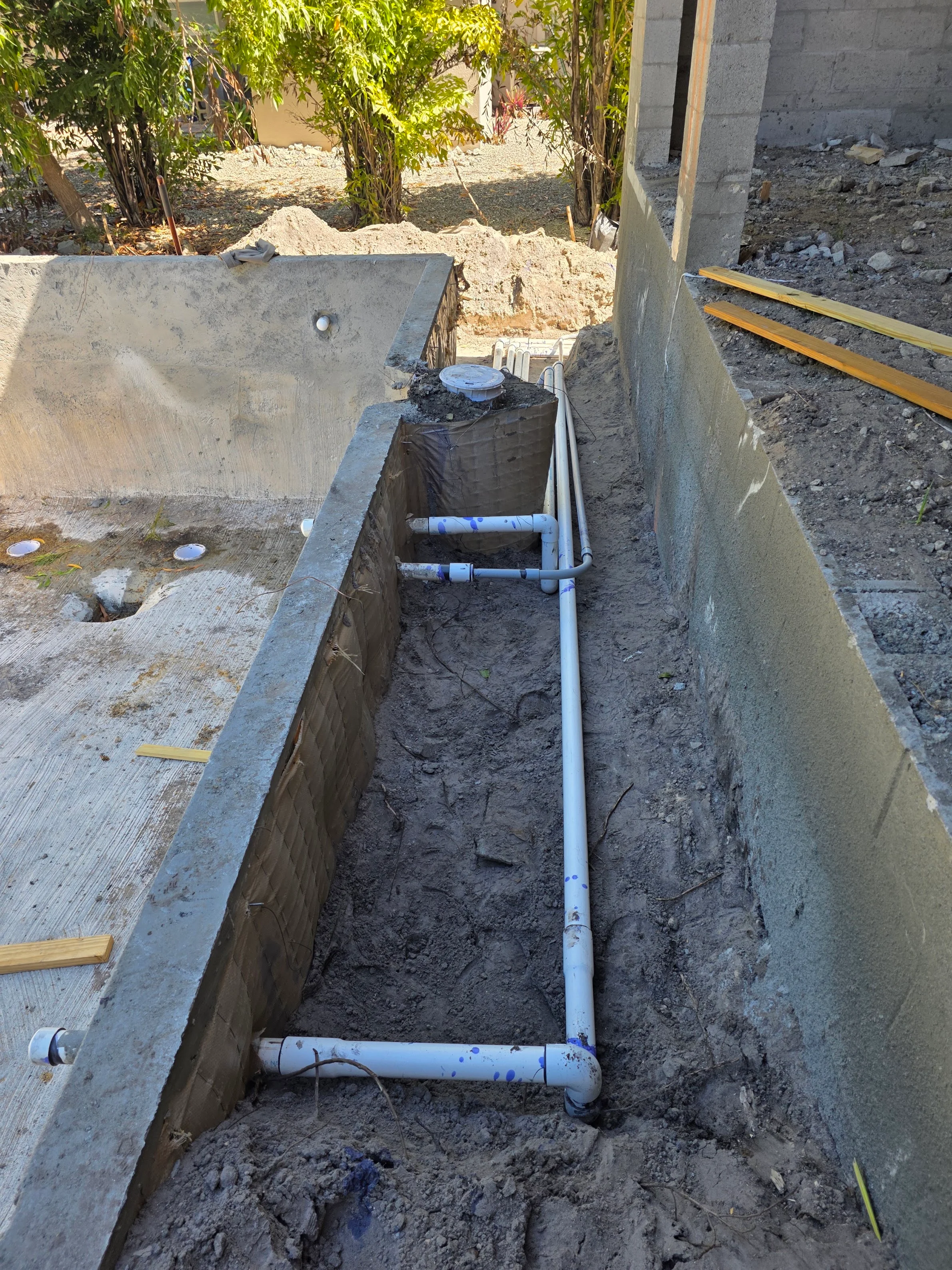 Underground PVC plumbing lines in concrete trench with blue and white drainage pipes