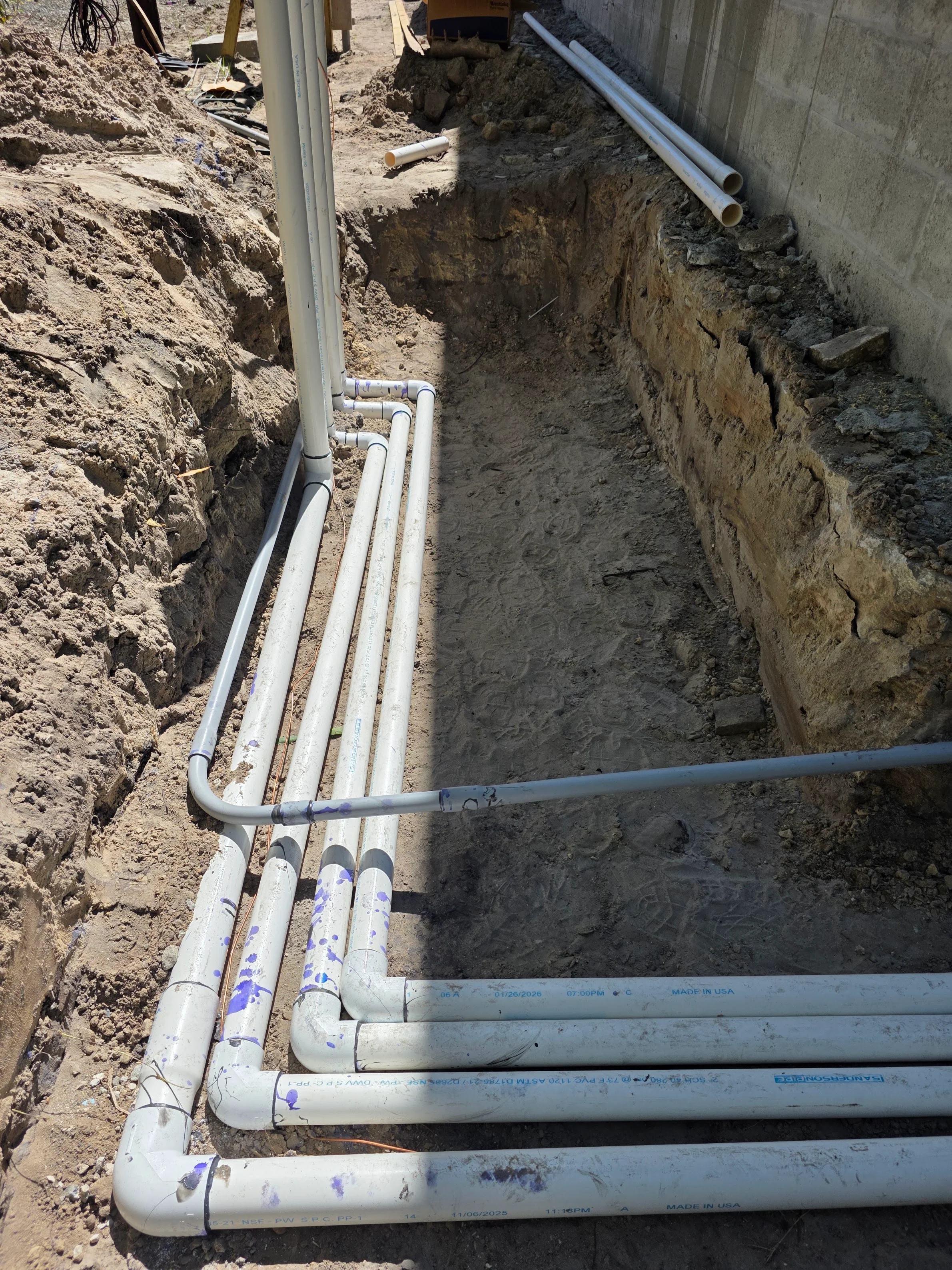 PVC pipes and fittings installed in excavated trench with concrete wall